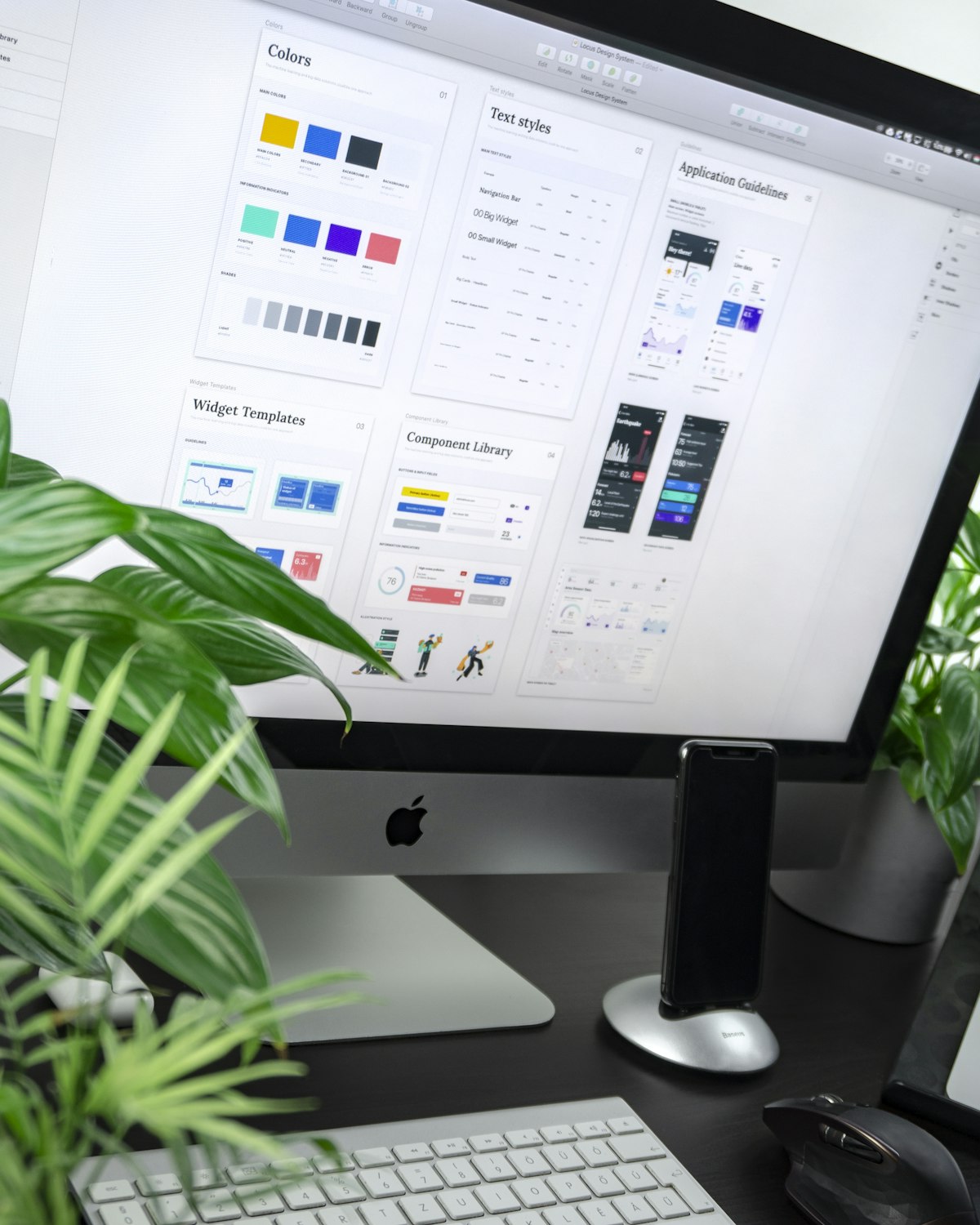 Skærm med designsystem, planter og mørkt skrivebord i et roligt atelier